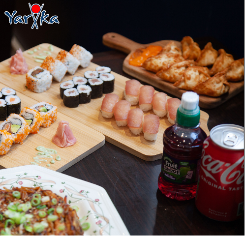 Yariika Sushi platter with maki rolls, nigiri, gyoza, and noodles, plus soda and a juice bottle.